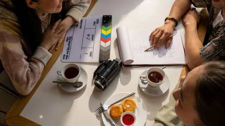 Discussion on a shoot , pre production, a clap board , camera, script, coffee, pen