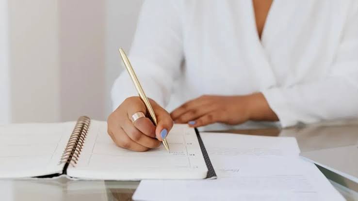 Women writing on a notebook with a golden pen and golden ring on her hand.