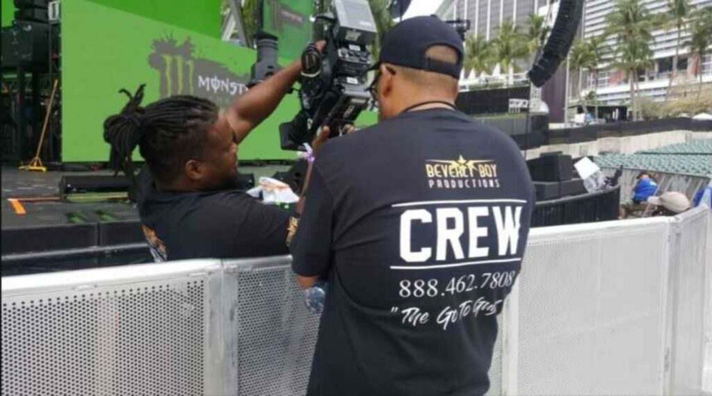 Video production crew members setting up camera equipment at an outdoor stage event.