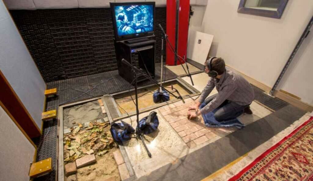 Foley artist recording sound effects using different surfaces and props in a soundproof studio.