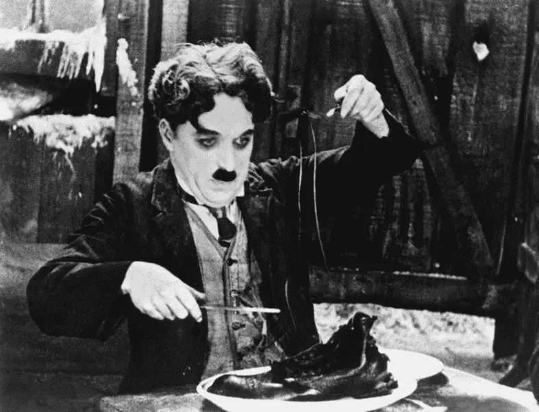 Charlie Chaplin eating a boiled shoe in The Gold Rush, a classic example of physical slapstick comedy in silent cinema.