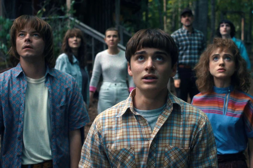 The main cast of Stranger Things Season 4 looking up in awe, demonstrating ensemble cast blocking and lighting direction.