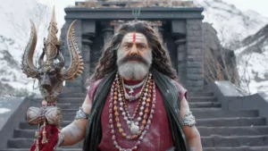 Balakrishna in a traditional Aghora look wearing Rudraksha beads and holding a Trishul in front of a snowy Himalayan temple in Akhanda 2.