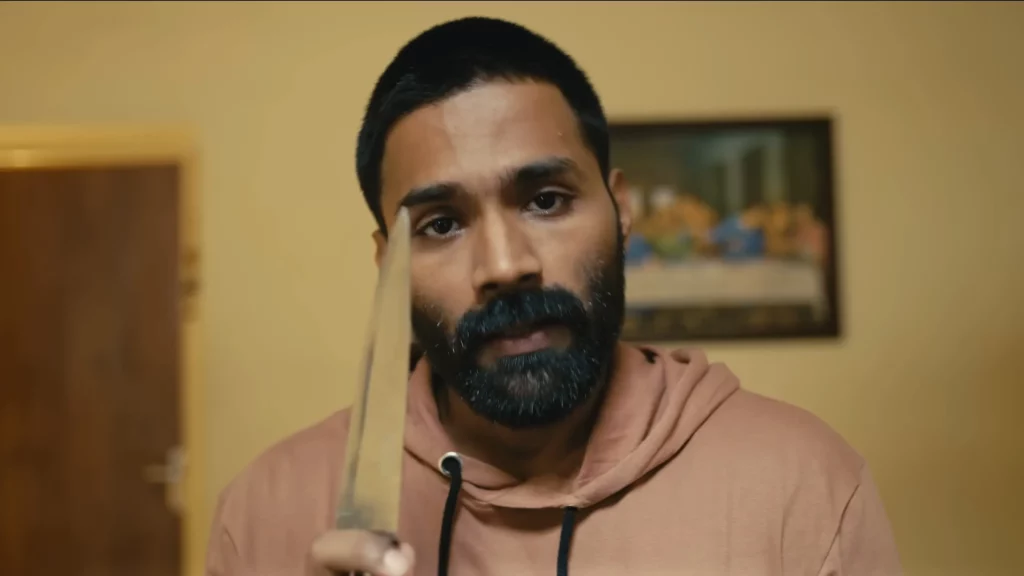 A close-up shot of actor Gomathi Shankar as the character Stephen, looking directly at the camera with an intense expression while holding a large knife near his face.