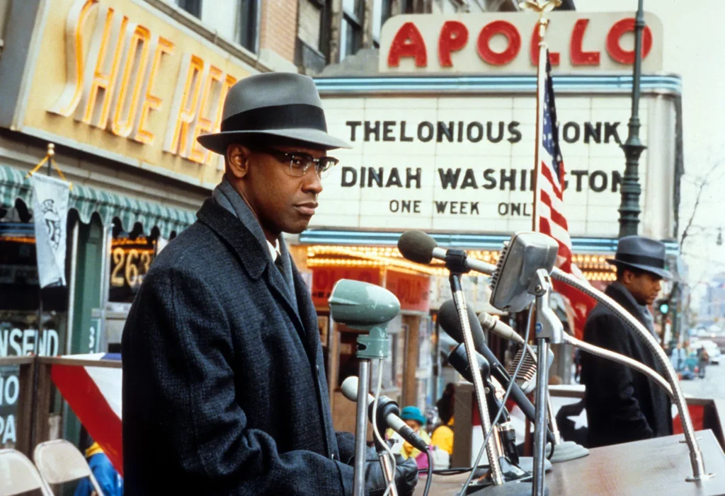 Actor Denzel Washington delivering a speech at a podium in front of the Apollo Theater in Spike Lee's film Malcolm X.