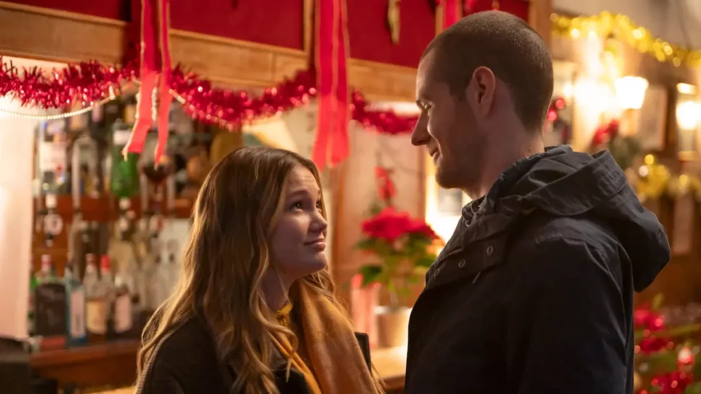 The lead characters of Jingle Bell Heist sharing a romantic moment in a decorated pub, showcasing the film's rom-com elements.