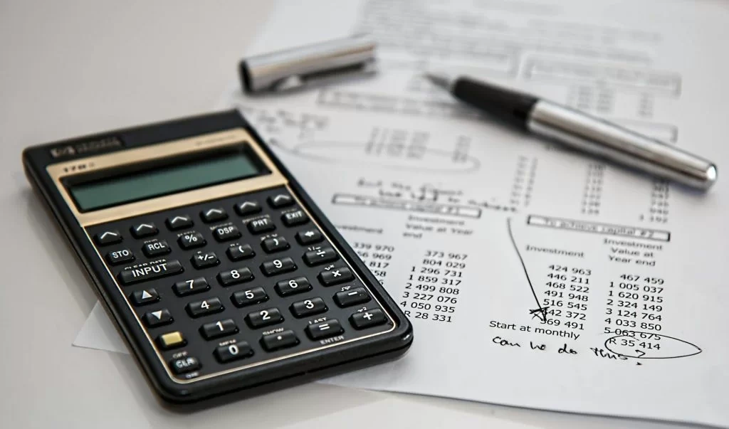 A close-up of a calculator, pen, and printed financial spreadsheet with handwritten notes, representing the detailed process of film budgeting and cost calculation.