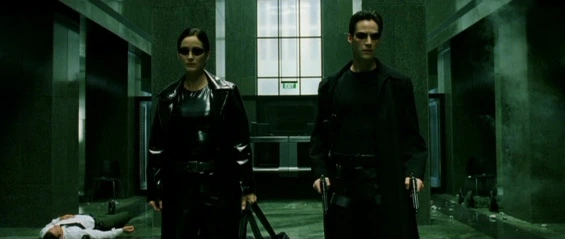 Trinity and Neo standing in the lobby in The Matrix, featuring the film's signature green tint used to distinguish the simulation from reality.