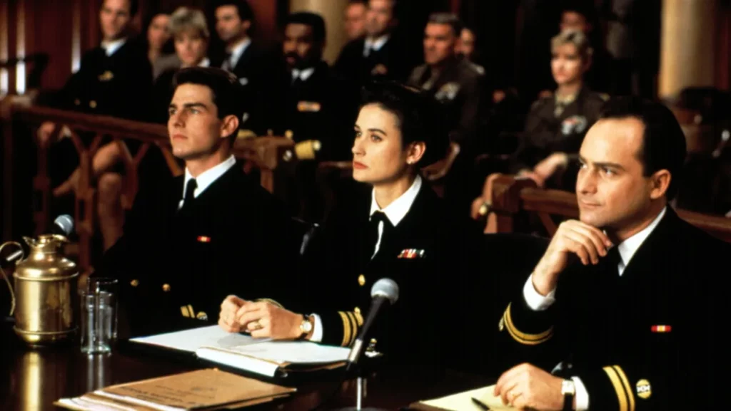 Tom Cruise, Demi Moore, and Kevin Pollak dressed in naval uniforms sitting together at a defense table in a courtroom scene from the movie A Few Good Men.