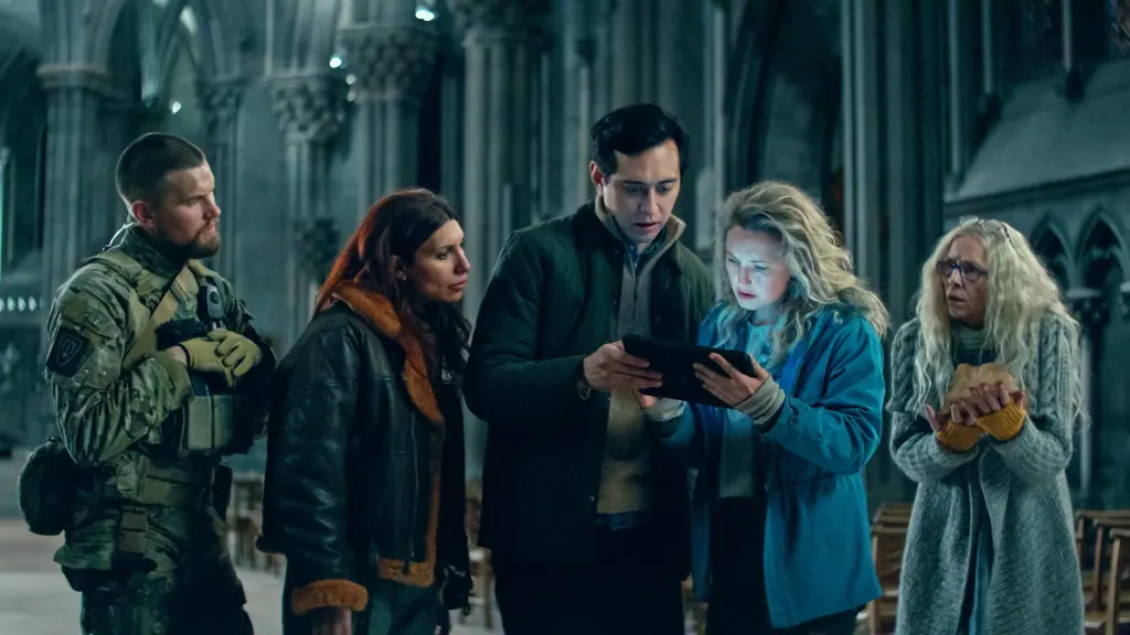 The main cast of Troll 2 movie (2025) looking at a tablet inside a stone church, including military personnel and scientists planning a strategy.