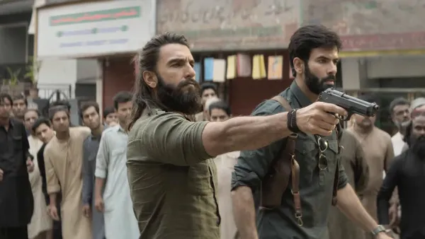 Ranveer Singh and a co-star holding a pistol walking through a crowded market street in an intense action sequence from Dhurandhar.