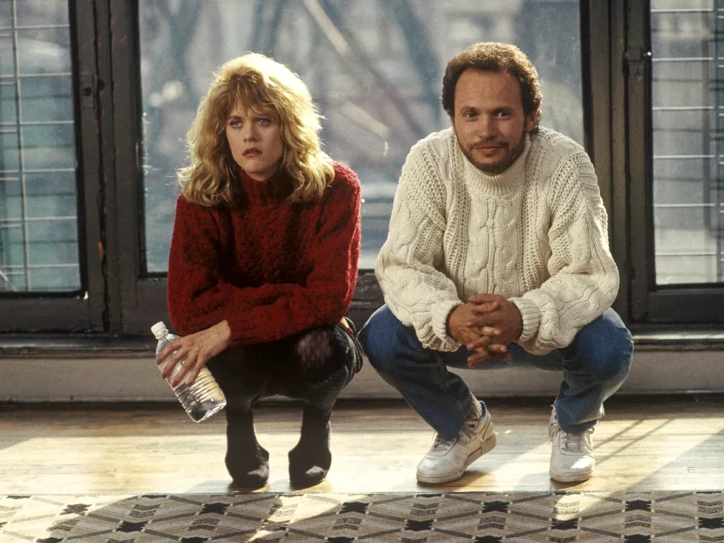 Meg Ryan and Billy Crystal squatting side-by-side in a scene from the movie When Harry Met Sally, with Ryan holding a water bottle.