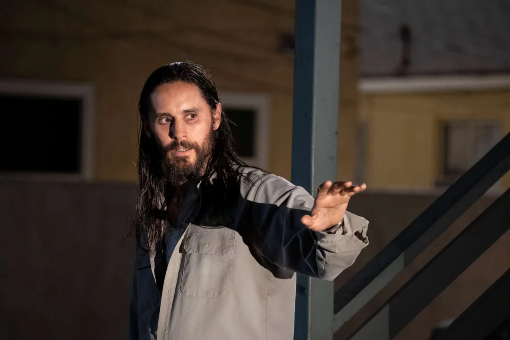 Jared Leto as the character Albert Sparma in The Little Things, with long dark hair and a beard, gesturing with his hand in a dimly lit setting.