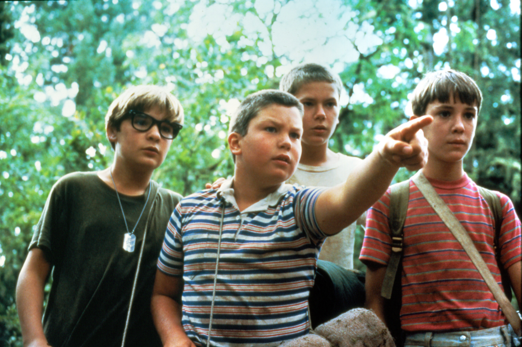 The four young main characters from the movie Stand by Me—including River Phoenix and Wil Wheaton—standing in a forest, with one boy pointing into the distance.