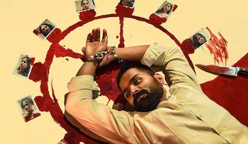 High-angle shot of the character Stephen lying on the floor with his hands handcuffed above his head, surrounded by a red painted circle containing photographs of female victims and a knife.