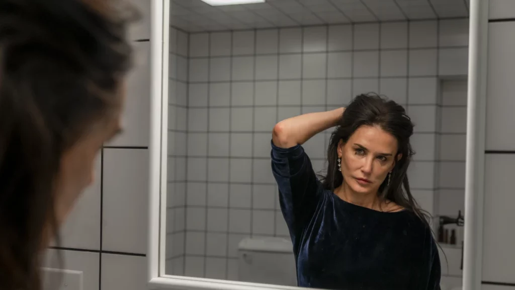 Demi Moore examining her reflection in a mirror in a scene from the body horror film The Substance.
