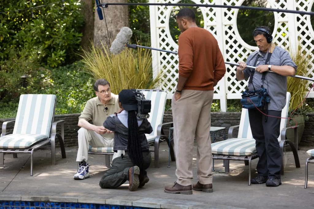Behind-the-scenes production still from The Staircase dramatized series showing Colin Firth as Michael Peterson being filmed by a crew with a boom mic and camera.