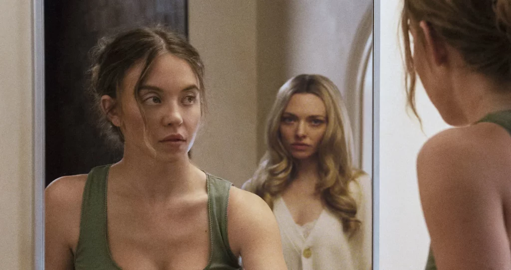 Woman staring into a mirror while another woman watches from behind, psychological thriller moment from The Housemaid