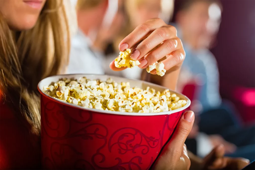 Woman eating popcorn at a movie theater, showing why popcorn became the iconic cinema snack why do we eat popcorn at movies