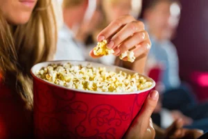 Woman eating popcorn at a movie theater, showing why popcorn became the iconic cinema snack why do we eat popcorn at movies