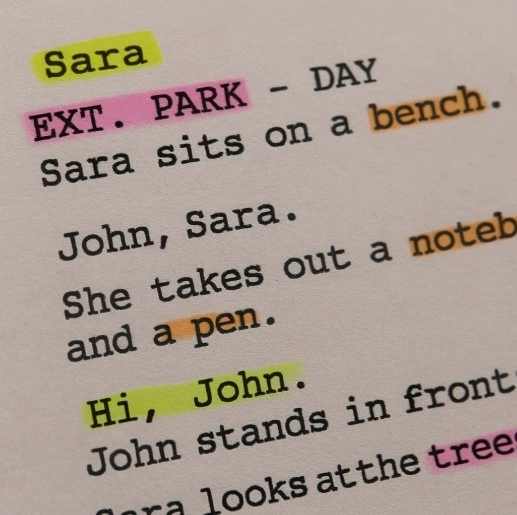 A close-up of a screenplay page marked with different colored highlighters indicating characters, props, and locations.
