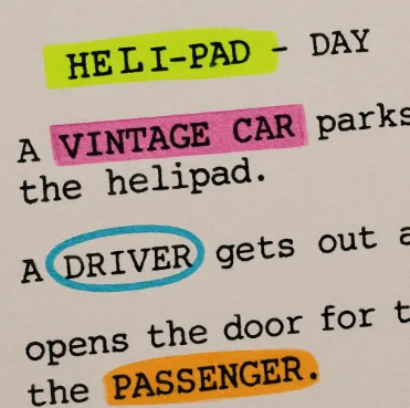 A close-up of a screenplay page with colorful digital highlights over words like 'HELI-PAD' and 'VINTAGE CAR'.