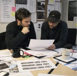 Two production team members analyzing pre-production documents and shot lists at a desk filled with film planning paperwork.