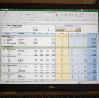 A laptop screen displaying a detailed movie budget breakdown spreadsheet with production cost tiers.